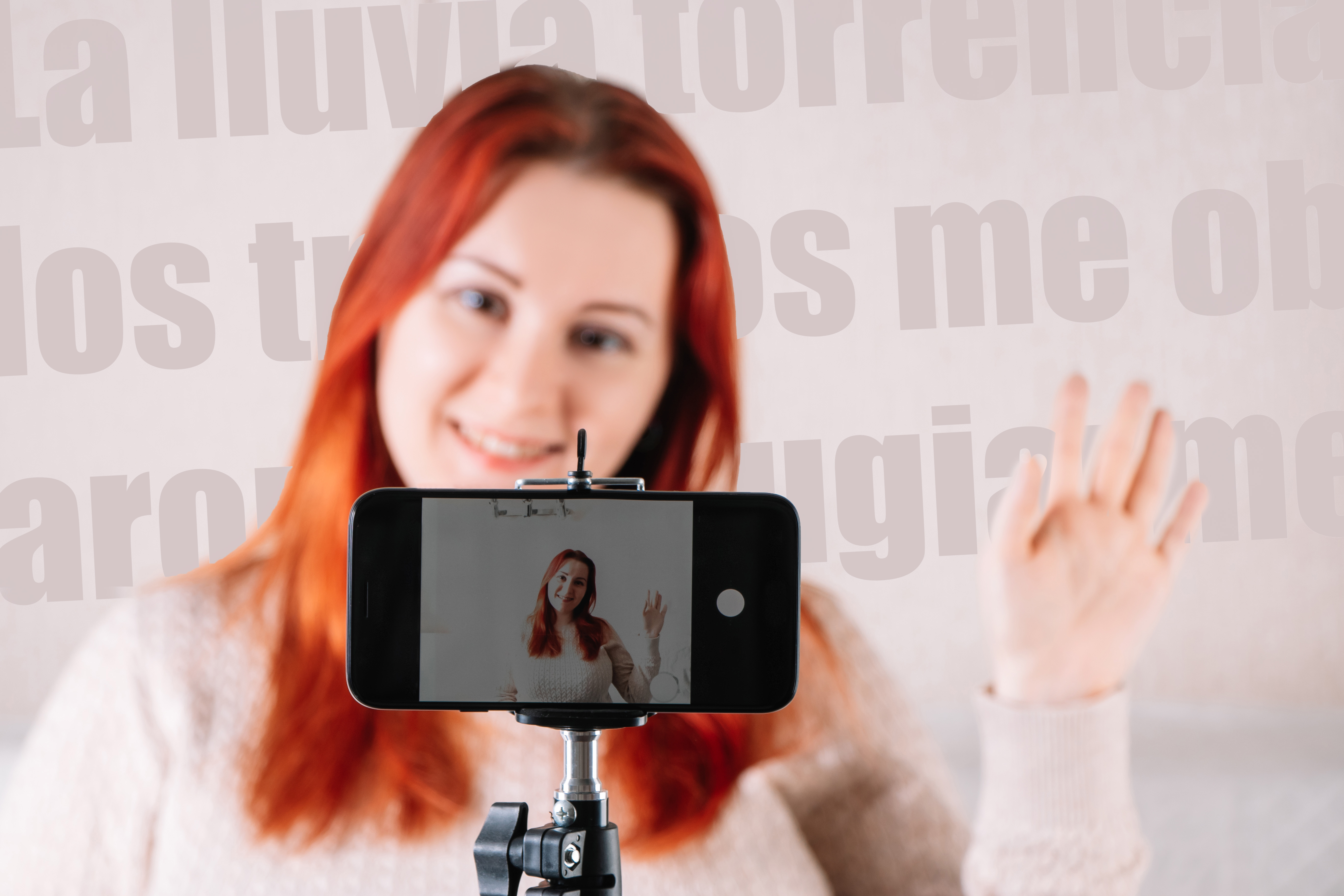 Young red-haired woman blogger leads an online stream using a smartphone. Influencer greets followers. The modern businesswoman works from home using social media.